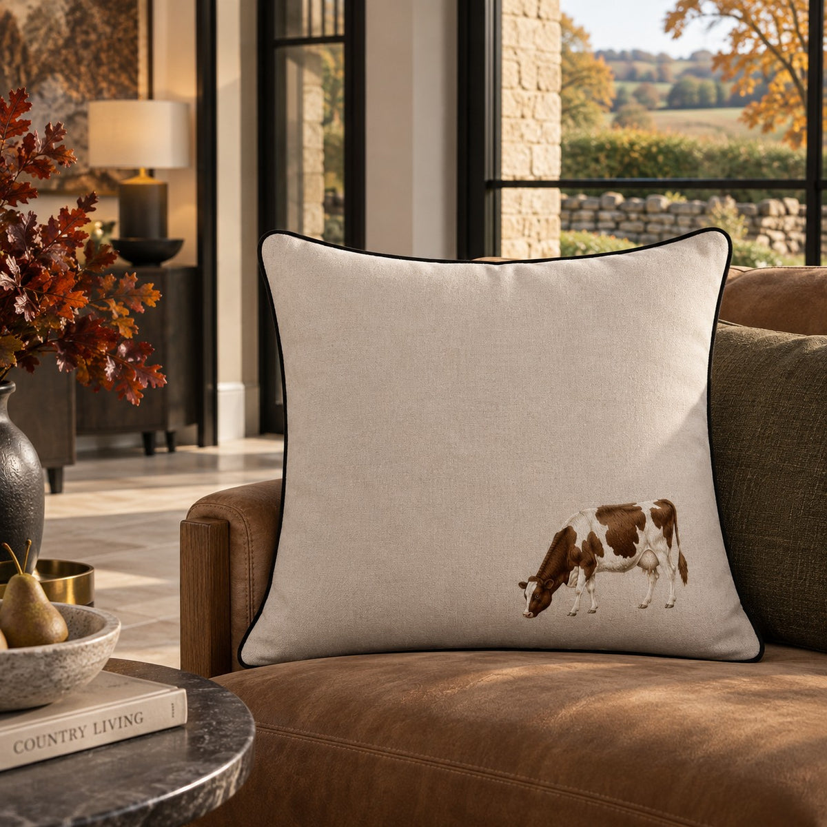The Meadow Cow Cushion from the Aminelle & Willow Country Edit, 50x50cm cotton linen cushion featuring an illustrated grazing cow with dark piping